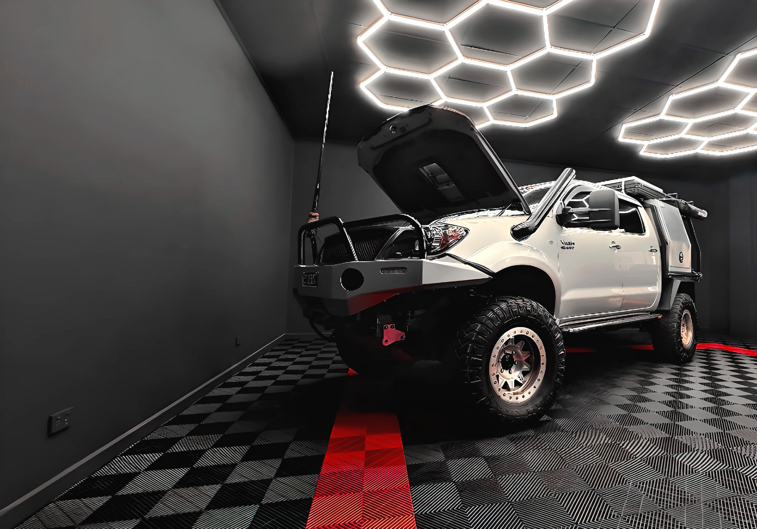 Silver SUV with open hood in a dark garage with geometric ceiling lights