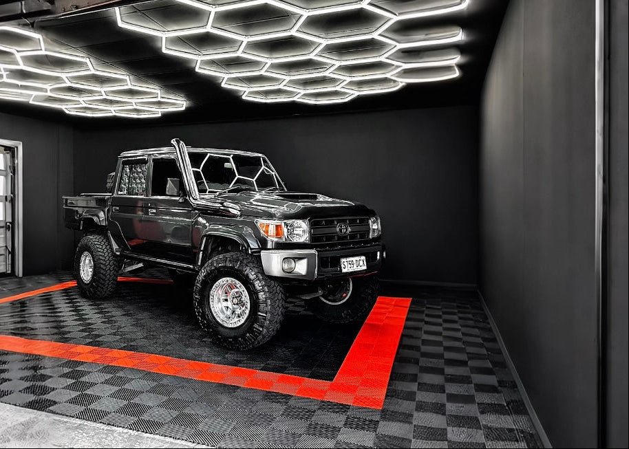 Black off-road vehicle inside a modern garage with geometric ceiling lights.